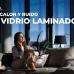 Mujer relajada en una sala moderna con grandes ventanales de vidrio laminado que aíslan el calor y el ruido exterior.